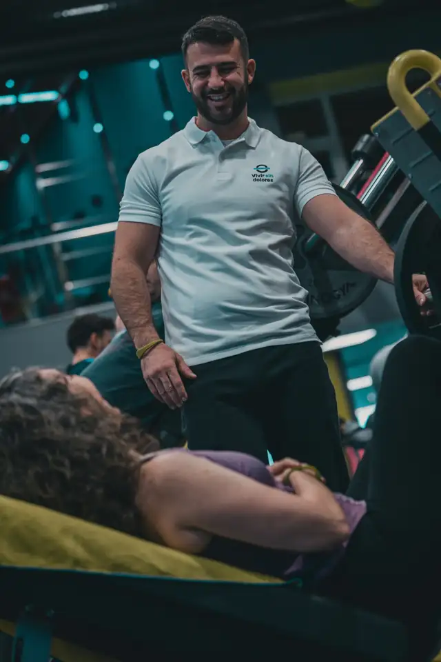 Personal trainer sorrindo enquanto auxilia uma aluna no treino