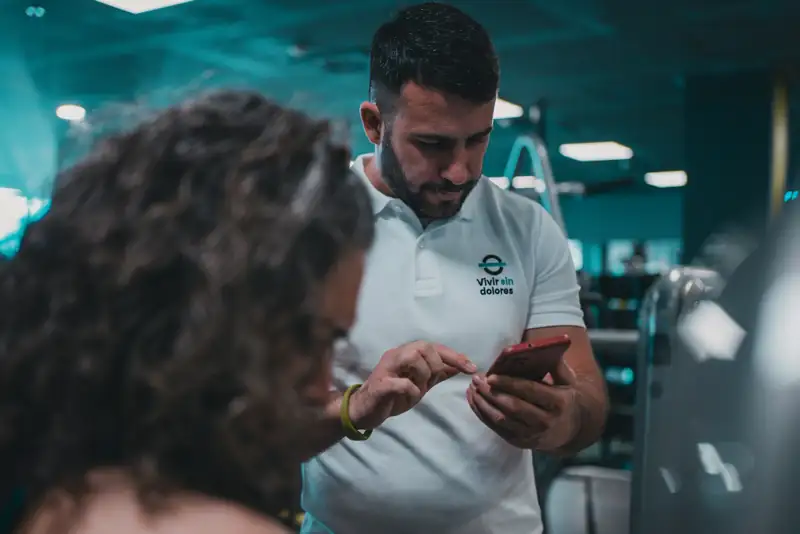 Personal trainer usando o celular na academia, ao lado de uma aluna